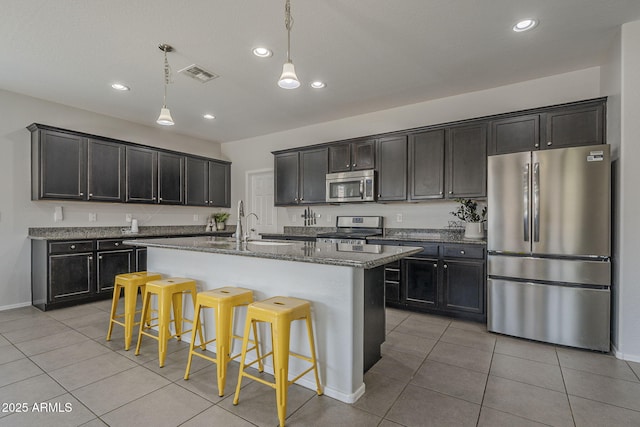 22463 E Desert Spoon Dr, Queen Creek, AZ 85142 - kitchen featuring appliances with stainless steel finishes, dark stone counters, light tile patterned floors, a kitchen bar, and hanging light fixtures