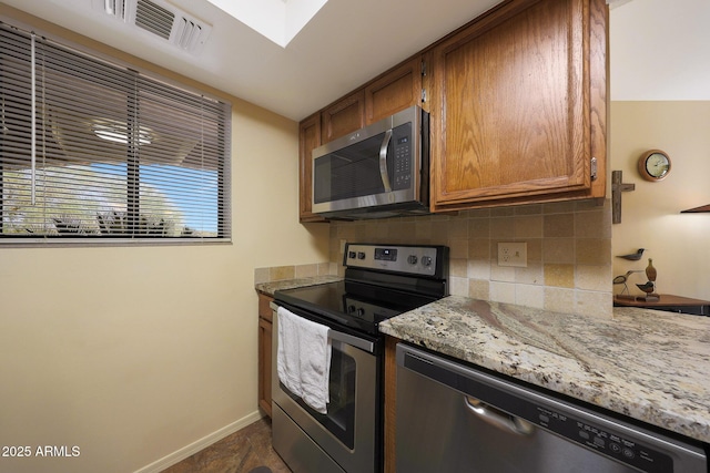 16108 E Emerald Dr Unit 106, Fountain Hills, AZ 85268 - kitchen featuring stainless steel appliances, decorative backsplash, brown cabinetry, light stone counters, and a skylight