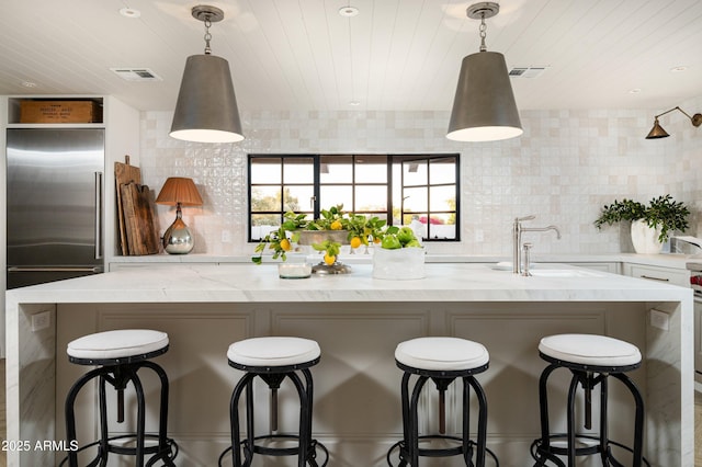 kitchen with decorative backsplash, a breakfast bar, a kitchen island with sink, and hanging light fixtures