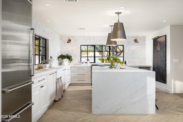 kitchen with built in refrigerator, light parquet flooring, hanging light fixtures, and white cabinets