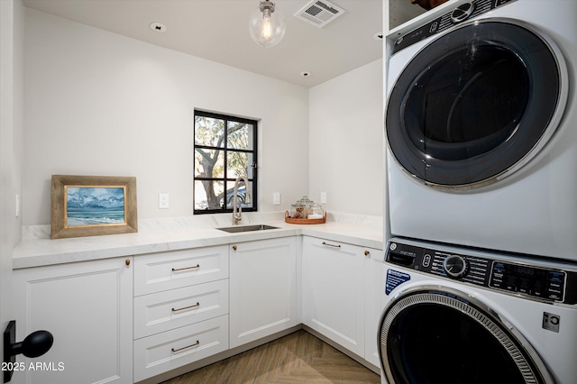 clothes washing area featuring cabinets, sink, stacked washer and clothes dryer, and light parquet floors