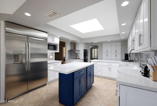 kitchen featuring built in appliances, white cabinetry, backsplash, and wall chimney exhaust hood