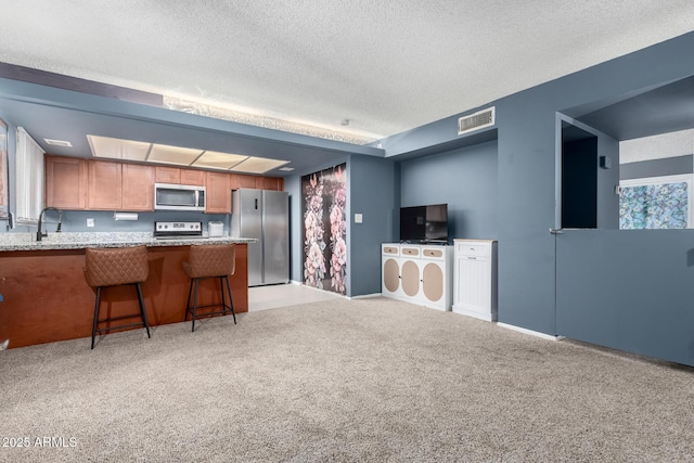 kitchen with stainless steel appliances, a textured ceiling, kitchen peninsula, a kitchen bar, and light colored carpet