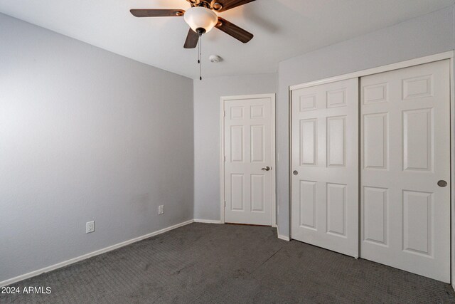 unfurnished bedroom with ceiling fan, dark colored carpet, and a closet