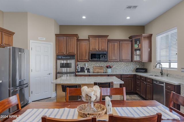 kitchen featuring sink, a center island, stainless steel appliances, light stone counters, and decorative backsplash