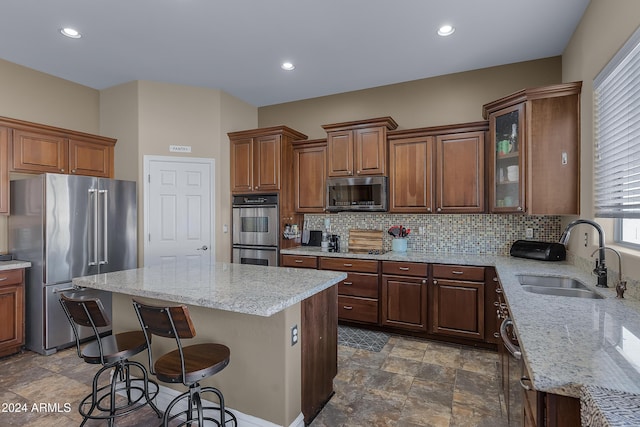 kitchen with sink, light stone countertops, appliances with stainless steel finishes, a kitchen island, and a breakfast bar area