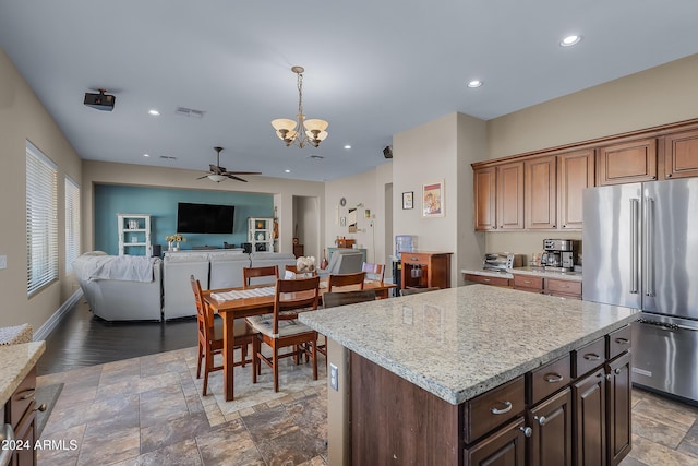 kitchen with light stone countertops, a center island, pendant lighting, high end fridge, and ceiling fan with notable chandelier