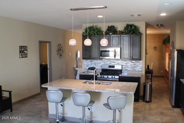 kitchen with decorative backsplash, light stone counters, appliances with stainless steel finishes, a kitchen breakfast bar, and a sink