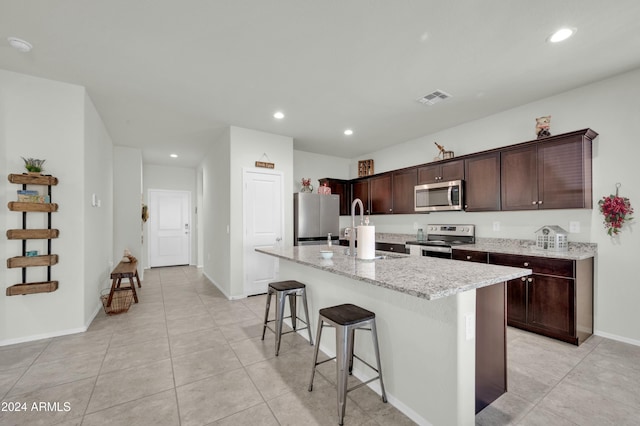 kitchen with sink, light stone counters, a kitchen bar, a center island with sink, and appliances with stainless steel finishes