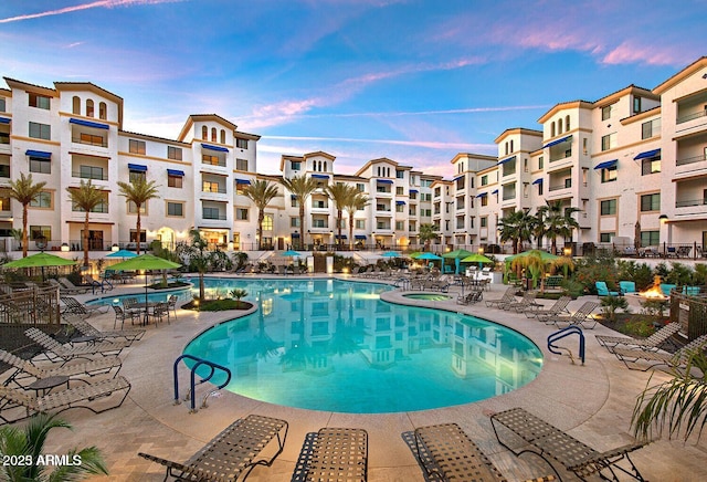 pool at dusk with a patio area and a community pool