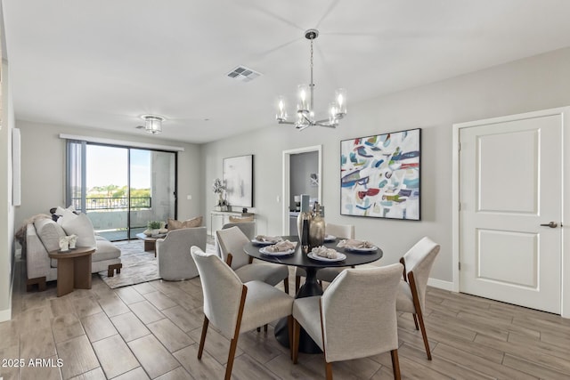 dining space with wood finish floors, visible vents, a notable chandelier, and baseboards