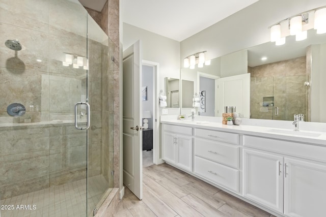 bathroom featuring double vanity, a shower stall, a sink, and wood finish floors