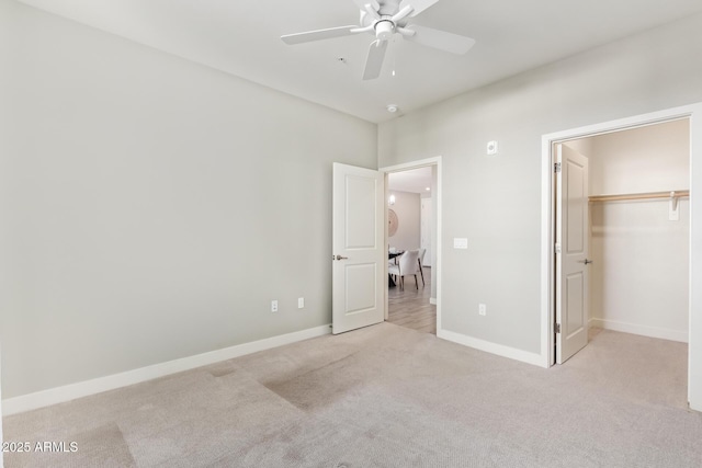 unfurnished bedroom featuring light carpet, ceiling fan, a walk in closet, and baseboards