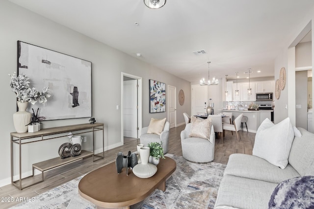 living area with an inviting chandelier, baseboards, visible vents, and light wood-style floors