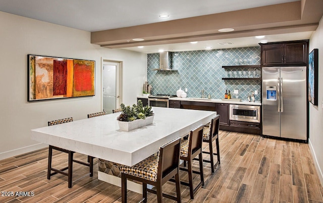 kitchen featuring stainless steel appliances, tasteful backsplash, light countertops, a sink, and wall chimney range hood