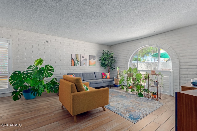 living room with brick wall, a textured ceiling, and light hardwood / wood-style flooring