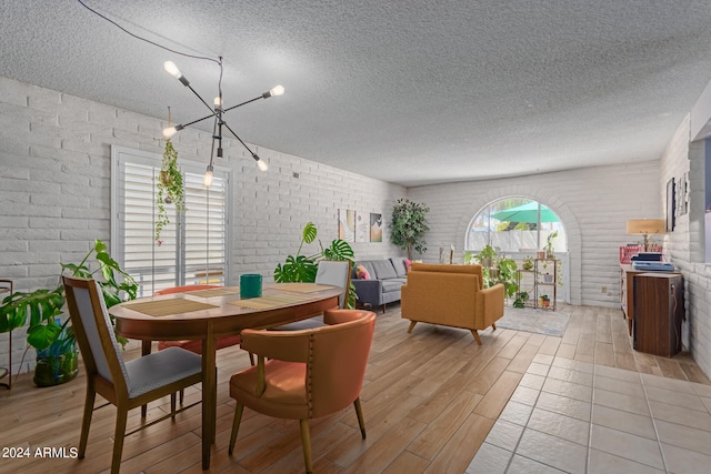 dining area featuring brick wall, a textured ceiling, light hardwood / wood-style flooring, and an inviting chandelier