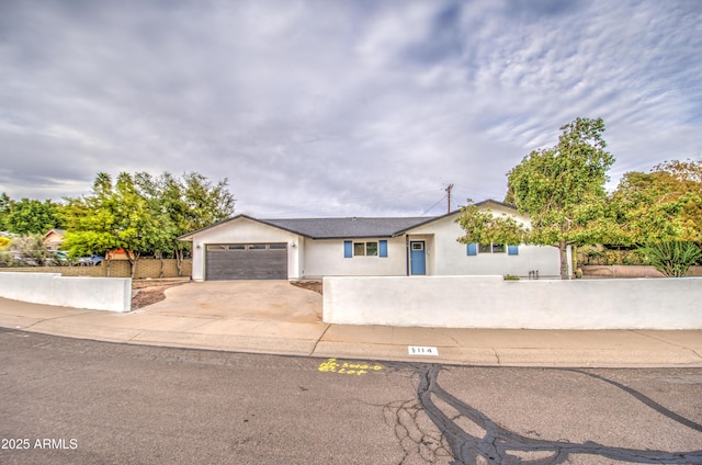 ranch-style home featuring a fenced front yard, concrete driveway, an attached garage, and stucco siding