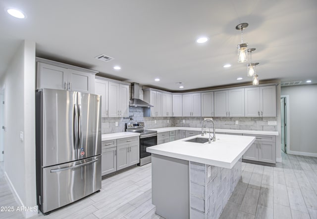 kitchen featuring light countertops, gray cabinetry, appliances with stainless steel finishes, a sink, and wall chimney range hood