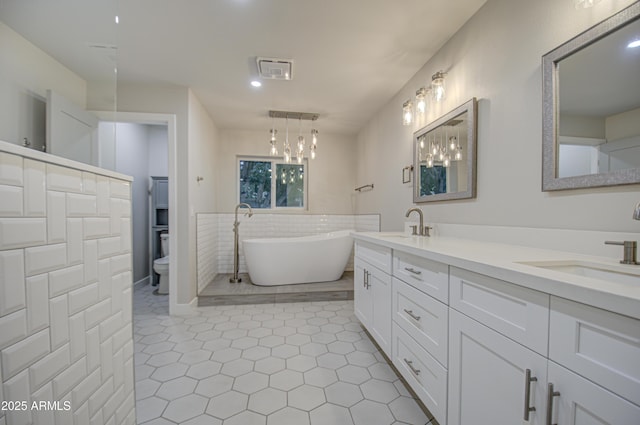 full bathroom featuring double vanity, toilet, a soaking tub, a sink, and tile walls