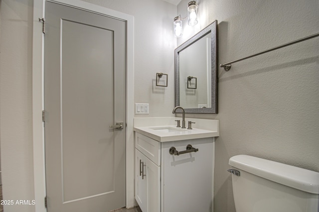 bathroom featuring toilet, a textured wall, and vanity