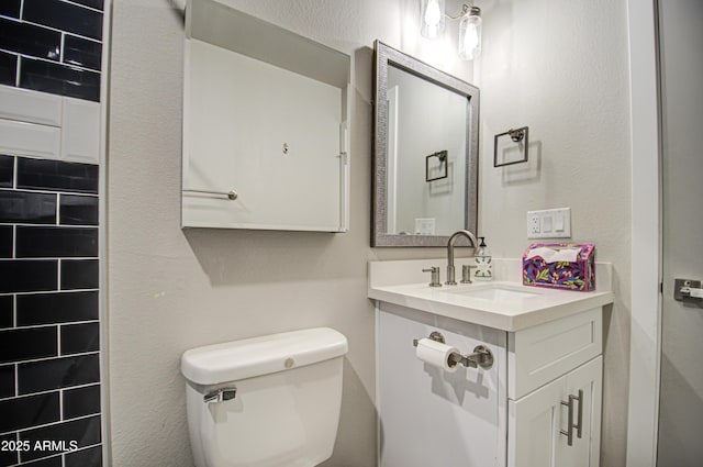 half bathroom featuring a textured wall, vanity, and toilet