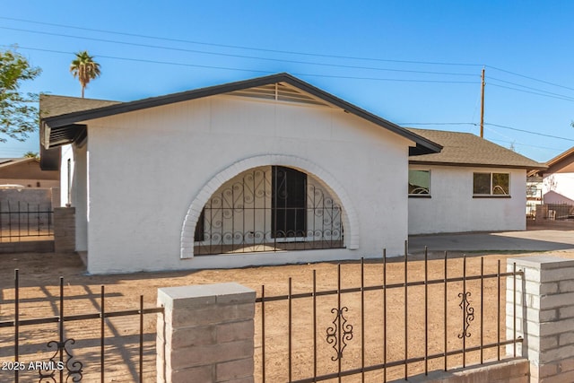 view of front facade with a fenced front yard, stucco siding, and roof with shingles