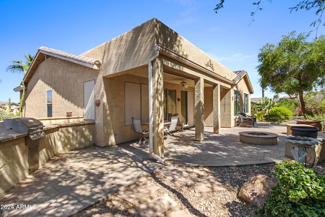 back of property with an outdoor fire pit, ceiling fan, a patio area, and an outdoor kitchen