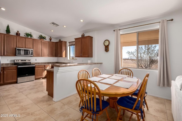 kitchen with lofted ceiling, a peninsula, visible vents, appliances with stainless steel finishes, and brown cabinetry