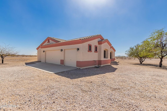 view of side of property with driveway, a tiled roof, an attached garage, and stucco siding