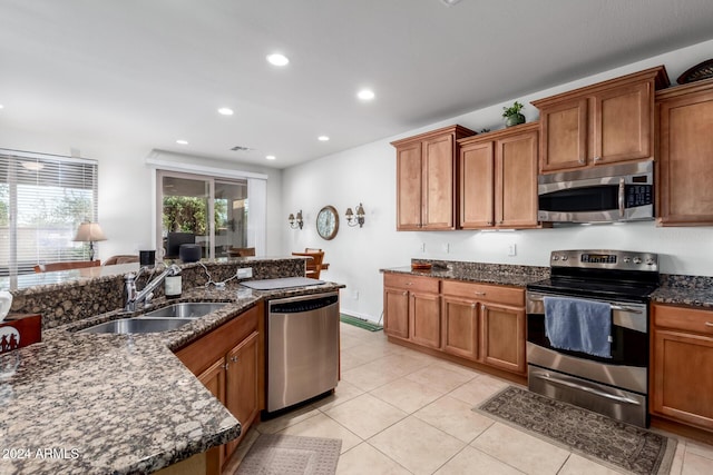 kitchen with appliances with stainless steel finishes, light tile patterned floors, dark stone counters, and sink