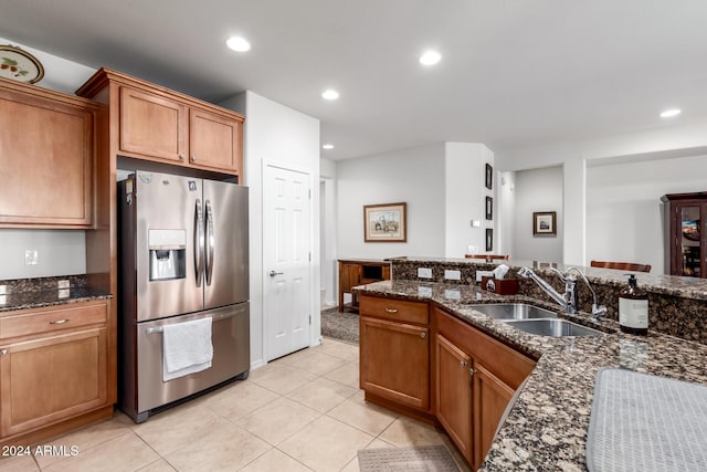 kitchen with stainless steel fridge with ice dispenser, light tile patterned floors, dark stone countertops, and sink