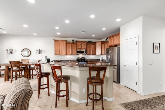 kitchen with a breakfast bar, light tile patterned flooring, dark stone countertops, and stainless steel appliances