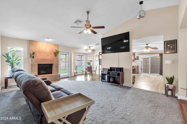 living room with a tiled fireplace, a wealth of natural light, vaulted ceiling, and hardwood / wood-style flooring