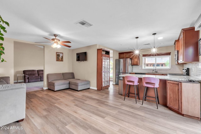 kitchen with stainless steel appliances, ceiling fan, backsplash, hanging light fixtures, and light hardwood / wood-style flooring