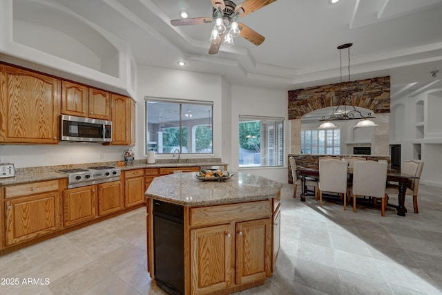 kitchen with appliances with stainless steel finishes, a tray ceiling, light stone countertops, a kitchen island, and decorative light fixtures