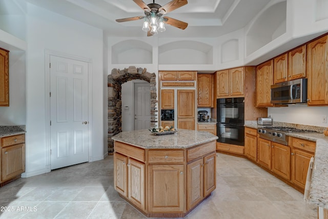 kitchen featuring light stone counters, a center island, ceiling fan, and appliances with stainless steel finishes