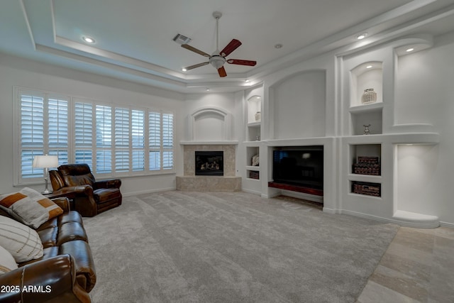 unfurnished living room with ceiling fan, built in features, a fireplace, and a tray ceiling