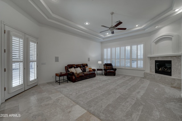 living room featuring ceiling fan, light colored carpet, a fireplace, and a tray ceiling