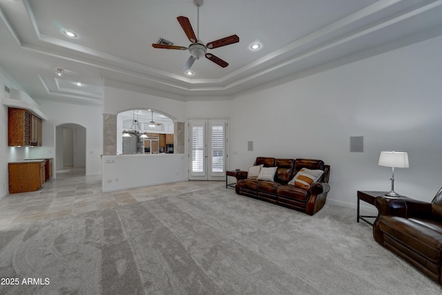 living room featuring a towering ceiling, light colored carpet, a raised ceiling, and ceiling fan