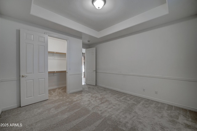 unfurnished bedroom featuring light colored carpet, a spacious closet, a raised ceiling, and a closet