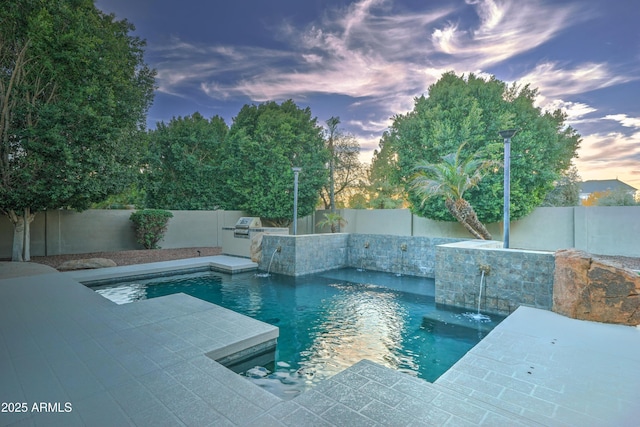 pool at dusk with a patio, pool water feature, and area for grilling