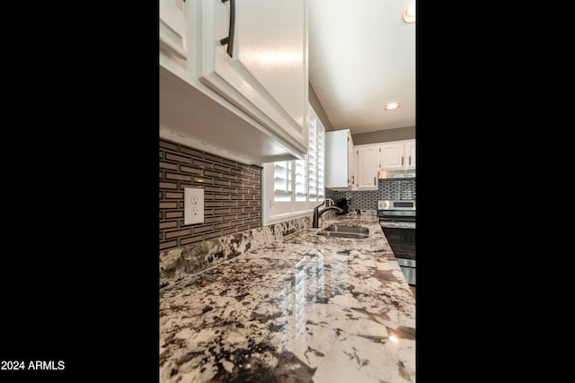 kitchen featuring tasteful backsplash, light stone counters, white cabinetry, sink, and stainless steel range oven