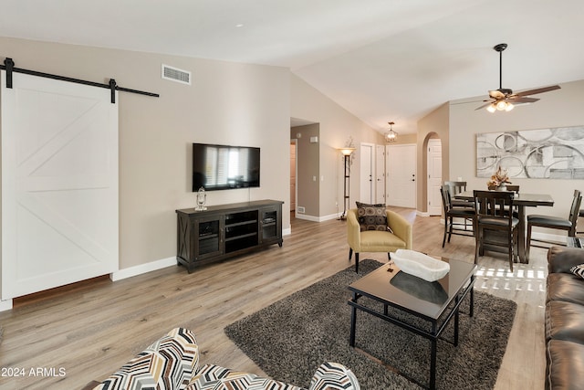 living room with a barn door, vaulted ceiling, ceiling fan, and light hardwood / wood-style flooring