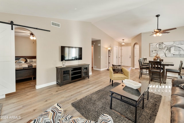 living room featuring light wood-type flooring, a barn door, vaulted ceiling, and ceiling fan