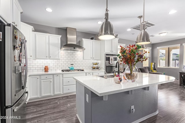 kitchen featuring white cabinets, appliances with stainless steel finishes, an island with sink, and wall chimney range hood