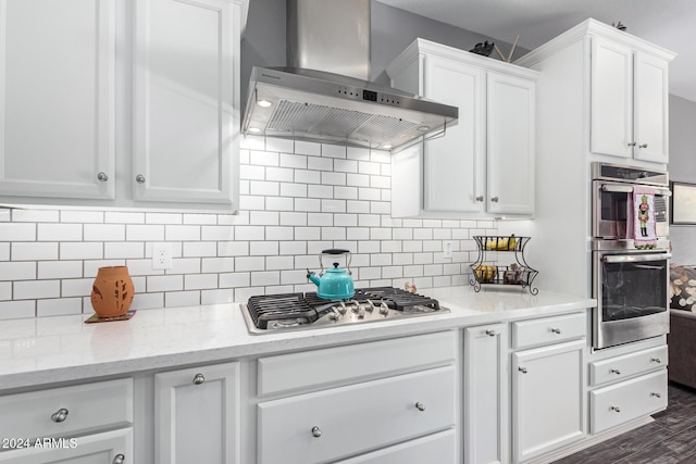 kitchen with white cabinetry, light stone counters, stainless steel appliances, decorative backsplash, and exhaust hood