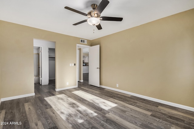 unfurnished bedroom featuring a closet, ceiling fan, dark hardwood / wood-style flooring, and a spacious closet