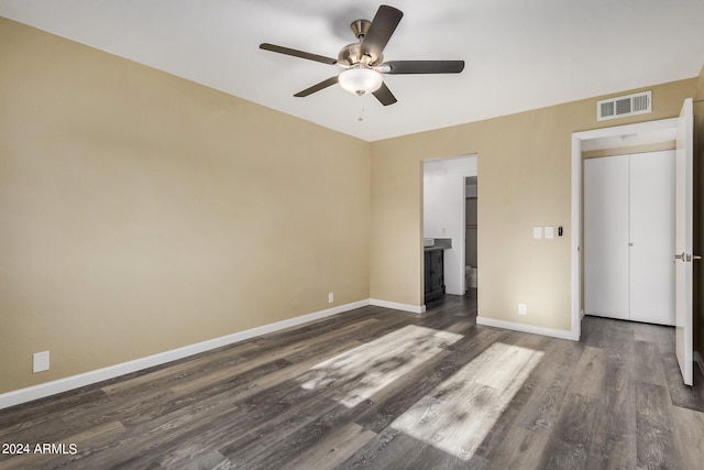 unfurnished bedroom featuring ceiling fan, dark hardwood / wood-style flooring, ensuite bath, and a closet