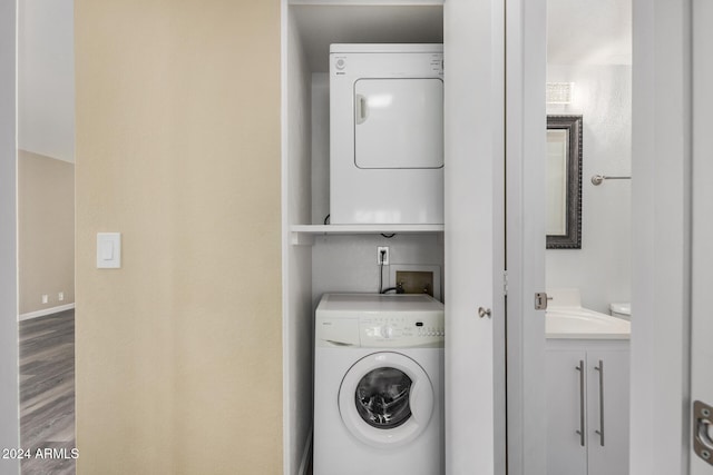 clothes washing area featuring hardwood / wood-style floors, stacked washer / drying machine, and sink